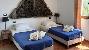 Une chambre avec deux lits, une tête de lit décorative en bois, une lanterne rouge et une fenêtre donnant sur un paysage verdoyant.