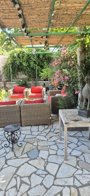 A covered outdoor seating area with wicker furniture and a stone floor.
