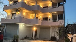 Un immeuble à plusieurs étages doté de balcons, d’un garage et d’une allée pavée de pierres.