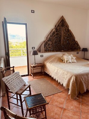 A bedroom with a bed, a chair, a small table, and a view of the outdoors.