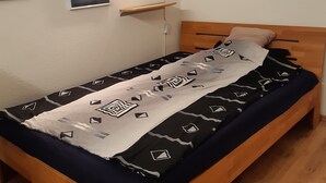 Una cama individual con una colcha estampada, cabecera de madera y una mesita de noche con lámpara.