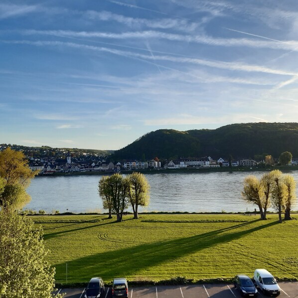 A parking lot with several cars, a grassy area, and a river with a town in the background. - Apartment with a view of the Rhine (Bad Hönningen)