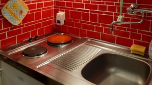 Una cocina con salpicadero de ladrillo rojo, electrodomésticos de acero inoxidable, un lavamanos y un grifo verde.