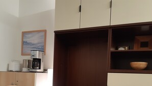 Una cocina compacta con encimera blanca, cafetera y repisa con un tazón.