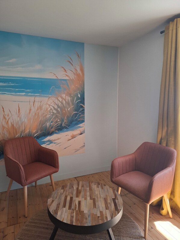 Ein Zimmer mit zwei Sesseln, einem runden Holztisch und einer Wandmalerei zum Strandthema.