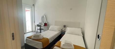 A hotel room with two beds, a desk, a chair, and a mirror.