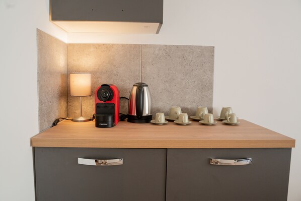 Una encimera de cocina con una cafetera, un hervidor, una lámpara y varias tazas.