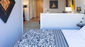 A hotel room with a bed, a desk, a chair, a small table with a lamp, and a wall with artwork. - Elegant Loft in Torremolinos Center with Pools, Near Beach and Nightlife (Torremolinos)
