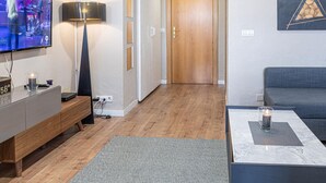 A modern living room with a flat-screen TV, a lamp, a sofa, and a wooden door in the background. - Elegant Loft in Torremolinos Center with Pools, Near Beach and Nightlife (Torremolinos)
