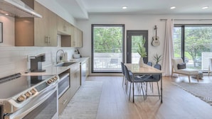 A modern kitchen with a dining area, large windows, and a view of the outdoors.