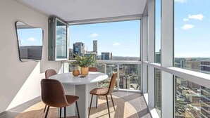 A modern dining area with a round table, chairs, and a city view through large windows. - Top Floor! 2Bed/2Bath/1Car/Pool/Views ~ CBD (Brisbane City)