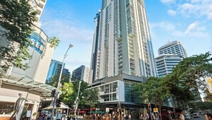 A tall, modern high-rise building with a glass facade, surrounded by urban streets and other buildings. - Top Floor! 2Bed/2Bath/1Car/Pool/Views ~ CBD (Brisbane City)
