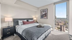 A bedroom with a bed, nightstand, lamp, and a city view through a large window. - Top Floor! 2Bed/2Bath/1Car/Pool/Views ~ CBD (Brisbane City)