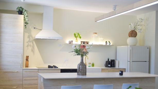 A modern kitchen with a central island, white chairs, and a vase of flowers.