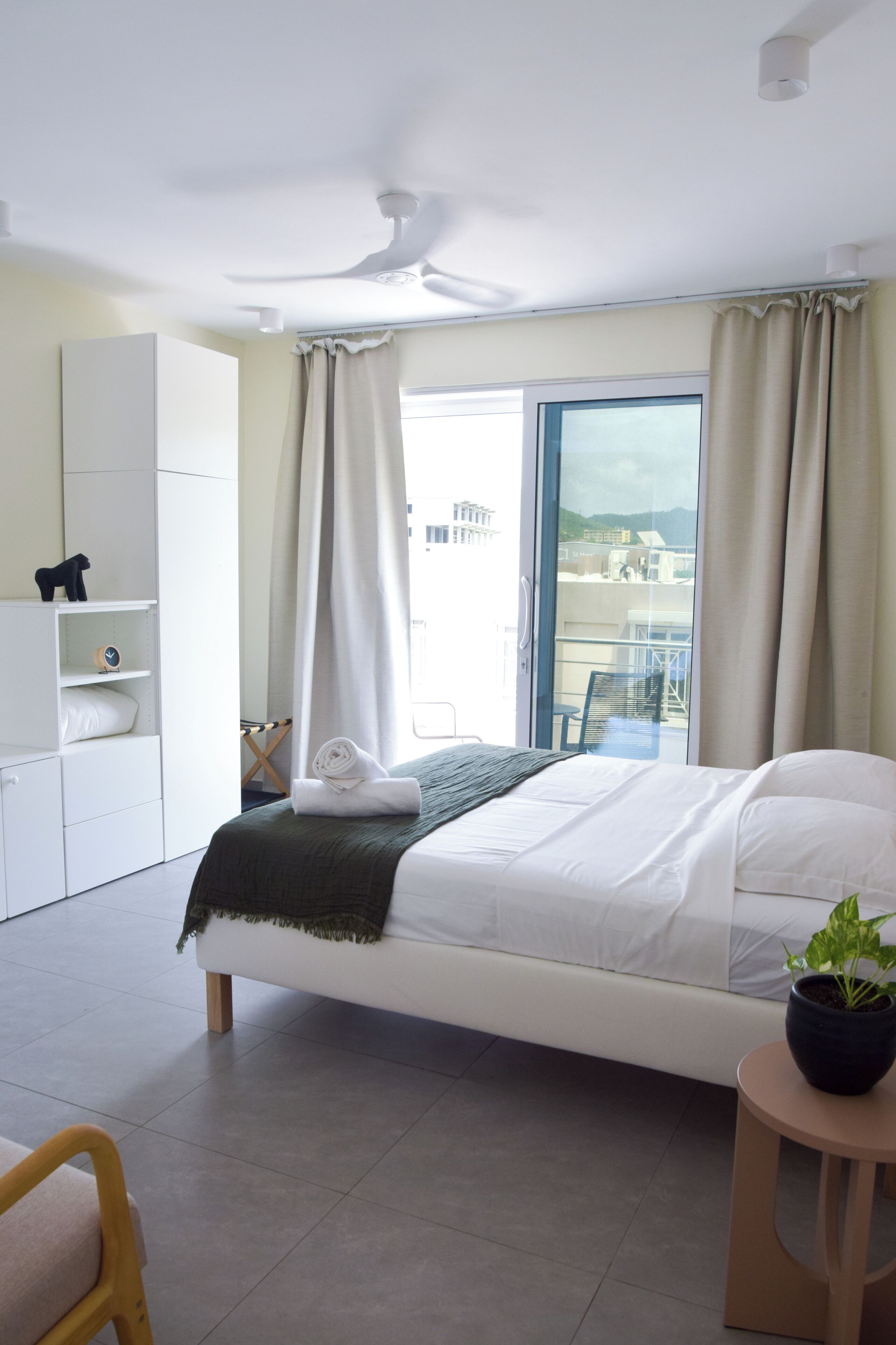 Ein modernes Hotelzimmer mit Bett, kleinem Tisch mit Pflanze, Kleiderschrank und Balkon mit Blick.