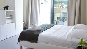 A modern hotel room with a bed, a small table with a plant, a wardrobe, and a balcony with a view.