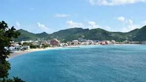 A coastal town with a beach, clear blue waters, and green hills in the background.