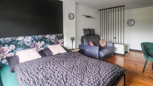A modern bedroom with a large bed, a sofa, a chair, a clock, and a decorative wall.