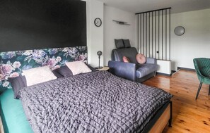 Une chambre moderne avec un grand lit, un canapé, un fauteuil, une horloge et un mur décoratif.