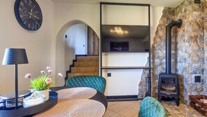 A living room with a clock, a fireplace, a staircase, and a modern light fixture.