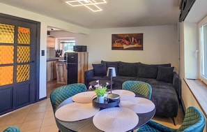 Un salon moderne avec un canapé foncé, une table basse ronde agrémentée de sets de table, et un coin repas avec des chaises.