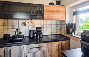 Une cuisine moderne avec un plan de travail noir, des meubles en bois, une machine à café et une fenêtre donnant sur un paysage verdoyant.