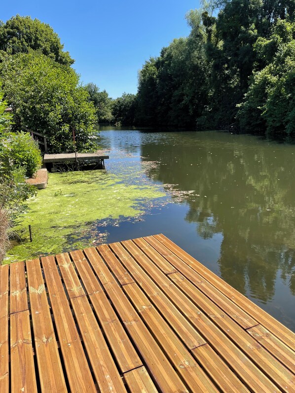 Eine Holzterrasse erstreckt sich über einen ruhigen Fluss, umgeben von üppiger Vegetation und Bäumen.