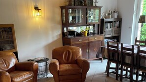 A cozy living room with a brown leather armchair, a wooden dining table, and a cabinet with glass doors.