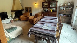 A cozy living room with a dining table, chairs, a sofa, a fireplace, and a wooden ceiling.
