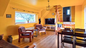 Una sala de estar acogedora con suelo de madera, un televisor y un comedor con mesa y sillas.