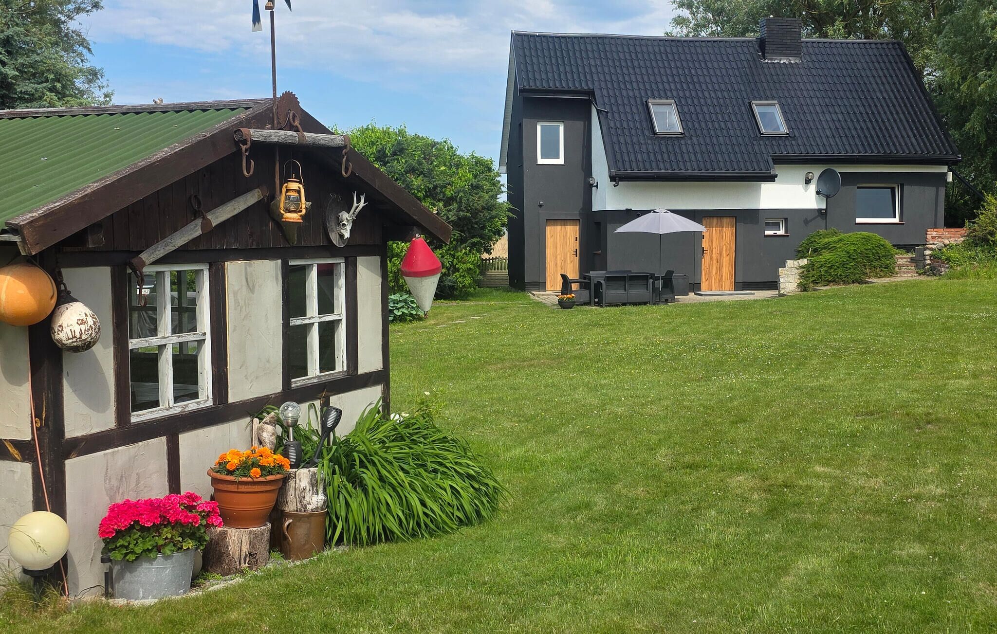Een traditioneel houten huis met een groen dak, een modern huis met een donker dak, en een gazon.