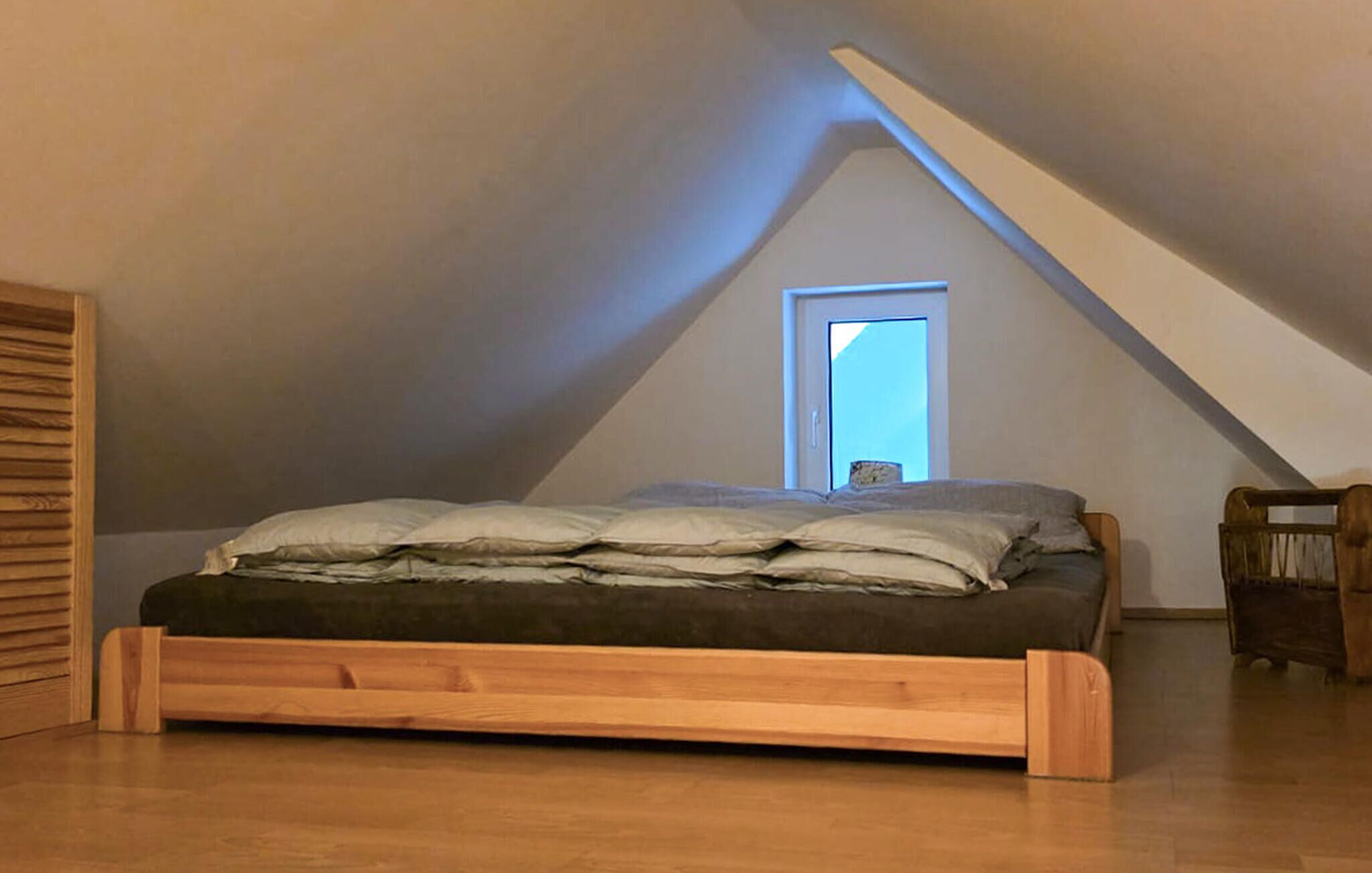 Une chambre à coucher aménagée dans un espace sous les toits, avec un plafond en pente, un cadre de lit en bois et une petite fenêtre.