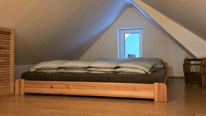 Un dormitorio tipo loft con techo inclinado, estructura de cama de madera y una ventana pequeña.