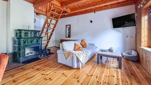 A cozy living room with a wooden ceiling, a sofa with cushions, a small table, a television mounted on the wall, and a wooden floor.