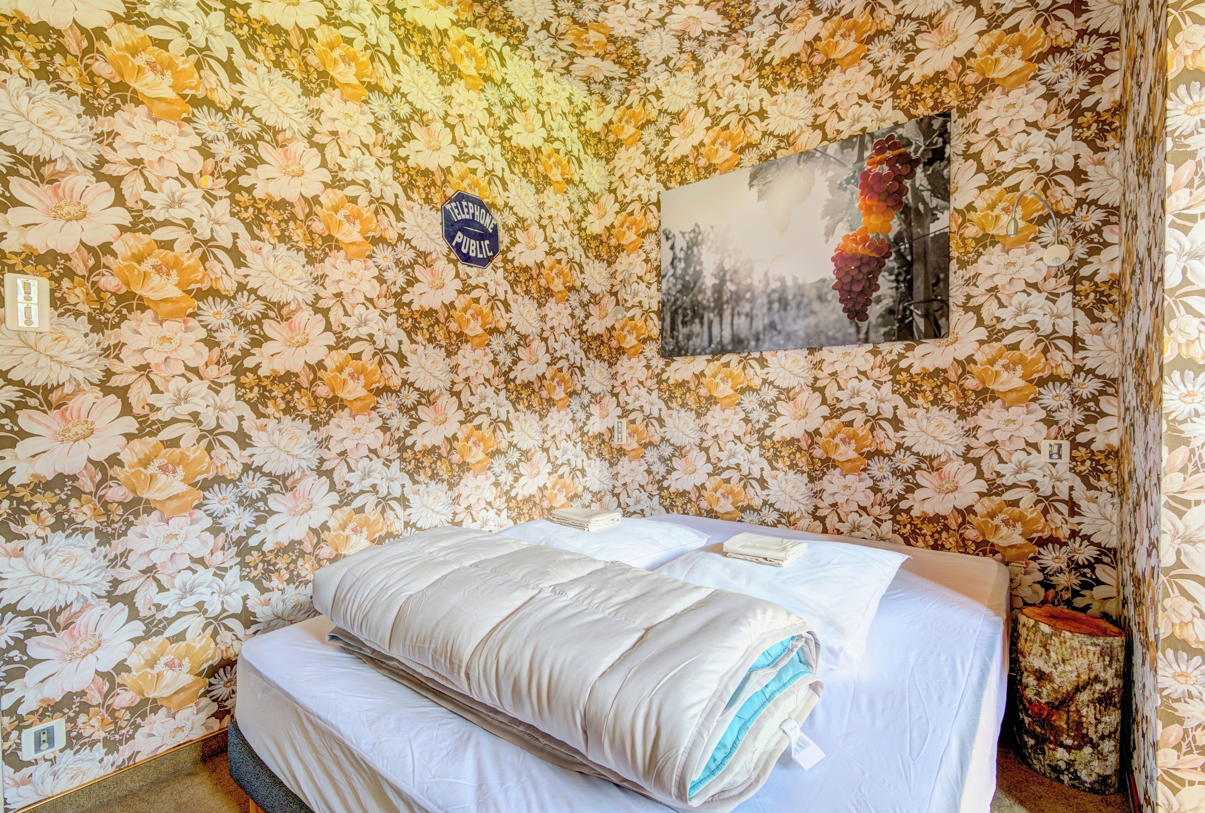 Une pièce dont les murs sont recouverts d’un papier peint à motifs floraux, un lit avec une couverture à rayures et un tableau encadré accroché au mur.