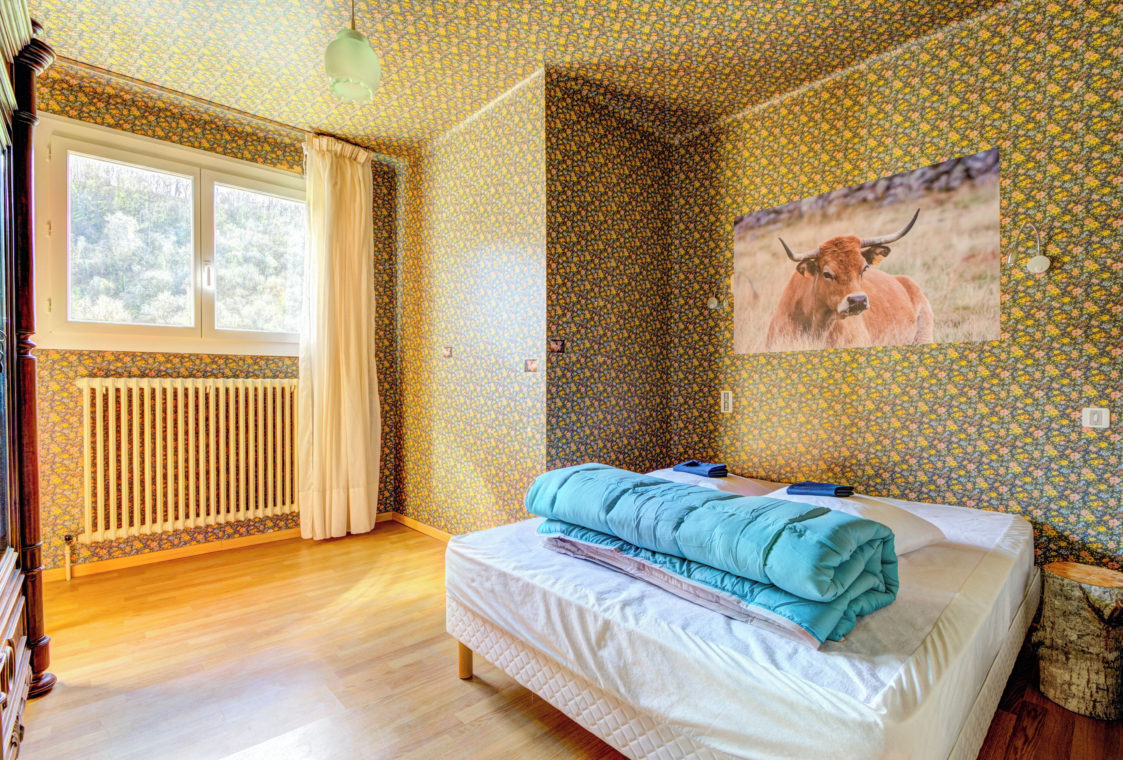A bedroom with a bed, a window, a radiator, and a wall with a floral pattern.
