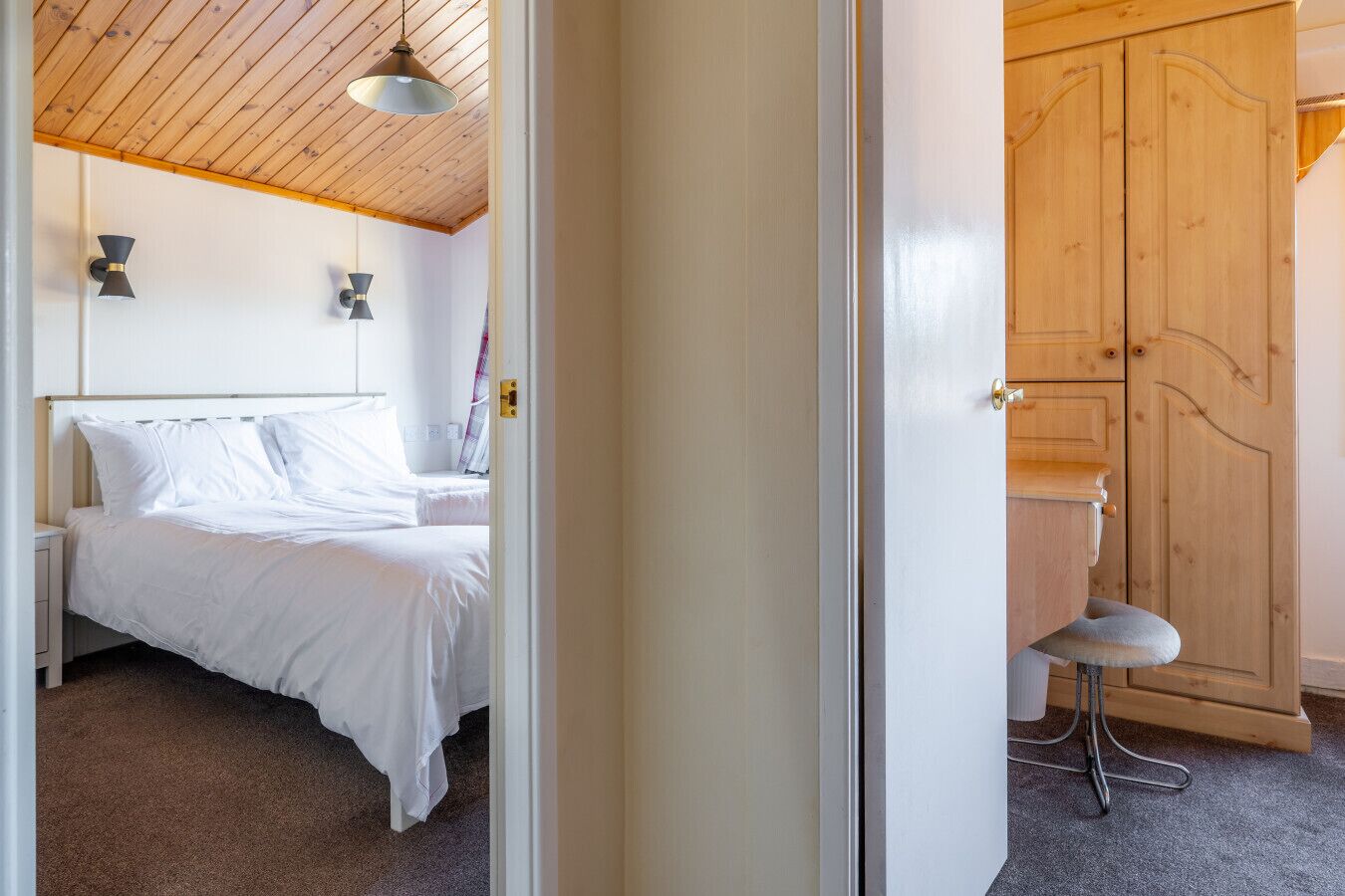 A bedroom with a bed, a bedside table, a lamp, and a wooden wardrobe.