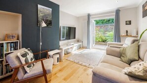 Una sala de estar moderna con un sofá, un televisor, una estantería y un ventanal que ofrece vistas al verdor.