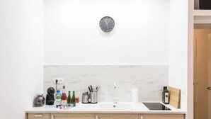 A kitchen with a white countertop, a sink, and a clock on the wall.