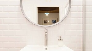 A bathroom with a white vanity, a round mirror, and a wooden cabinet.
