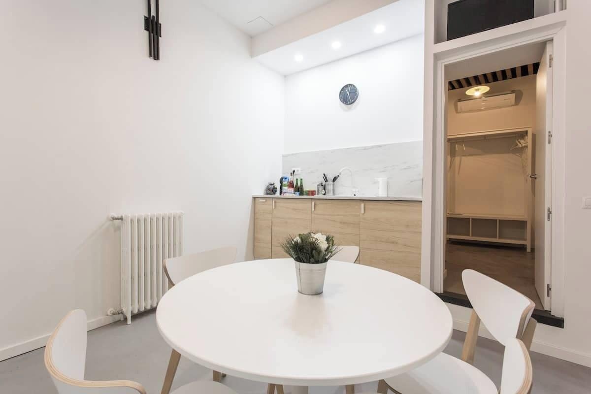 Una cocina moderna con armarios blancos, una mesa redonda de comedor y una planta en maceta.