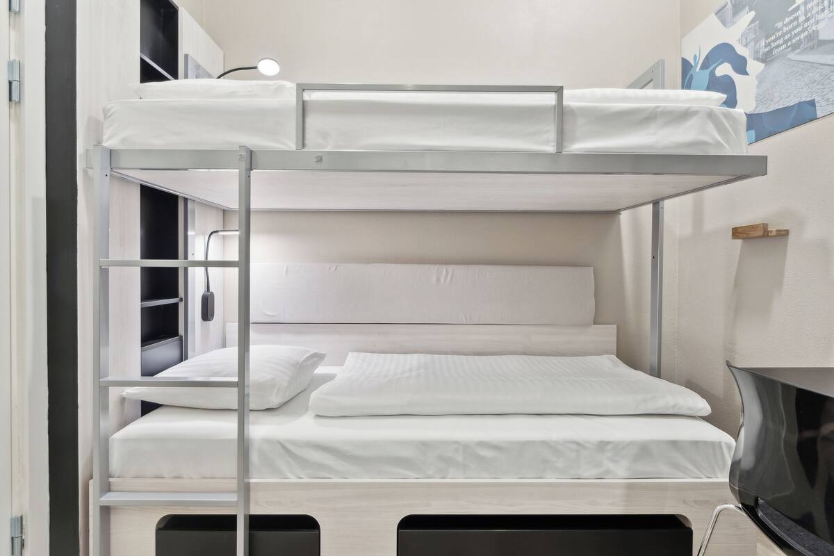 A bunk bed with white bedding and a desk area with a lamp.