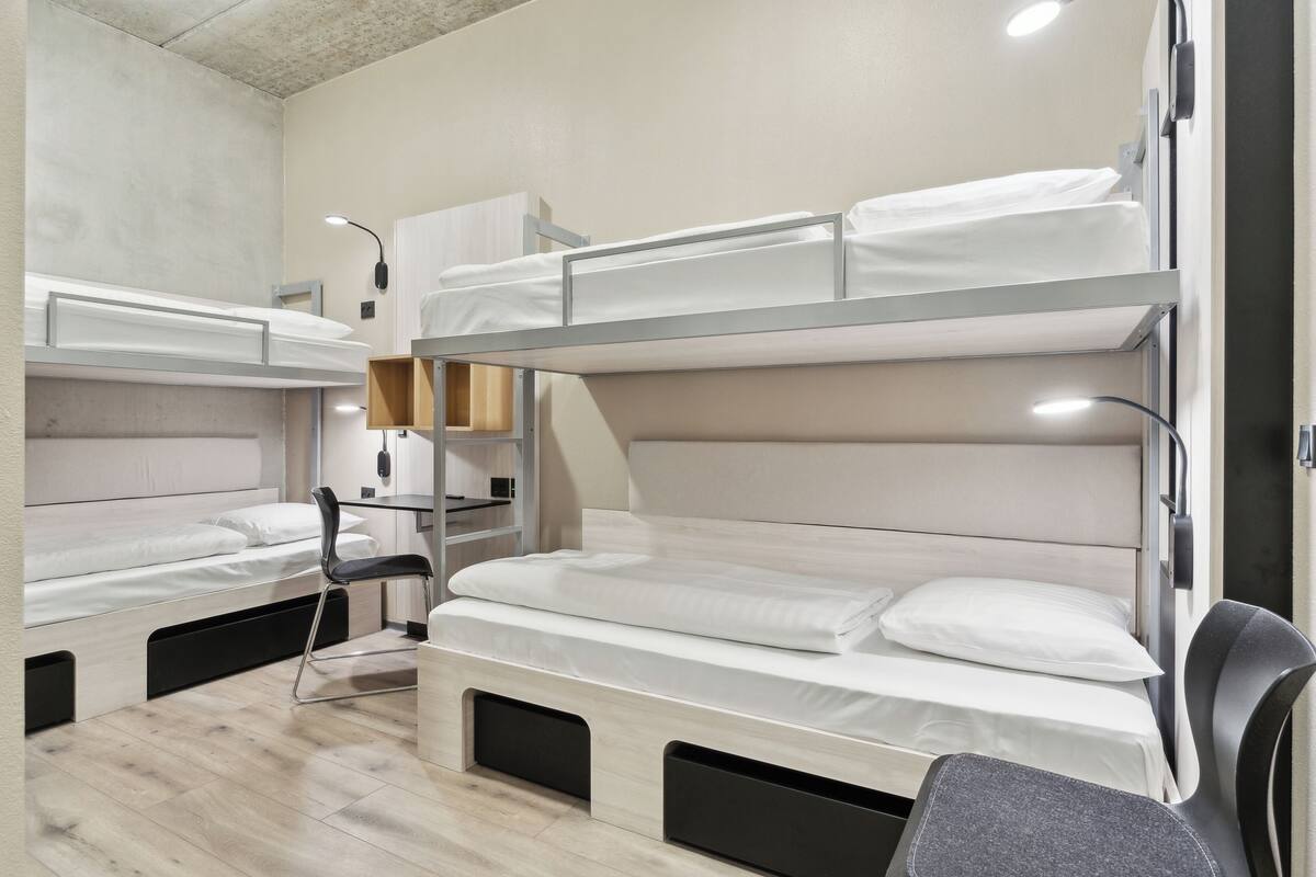A bunk bed room with a desk and chair, a lamp, and a small shelf.
