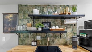 Une cuisine moderne avec un évier noir, un plan de travail en bois et des étagères où sont rangés des ustensiles de cuisine et des objets décoratifs.