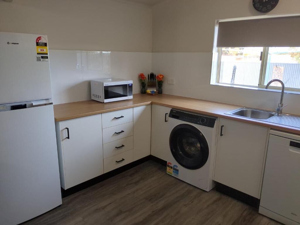 A compact kitchen with a microwave, washing machine, and sink.