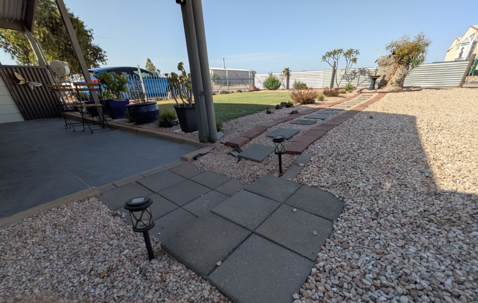 A patio area with a stone pathway, outdoor furniture, and a pergola structure.
