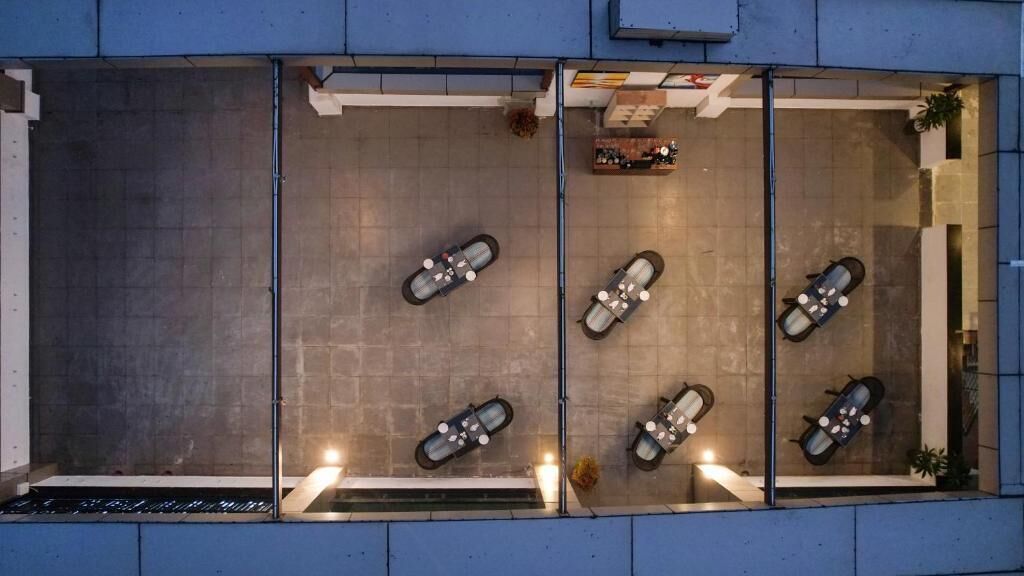 A top-down view of a restaurant with four tables, each with a chair. The restaurant has a modern design with a concrete floor and a glass partition separating the dining area from the rest of the space.