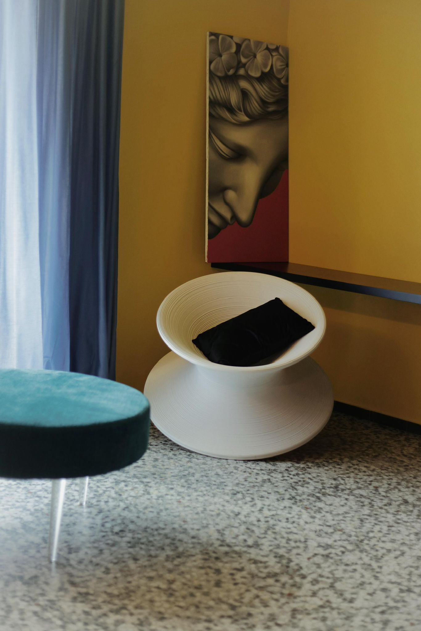 Een moderne kamer met een witte stoel, een ronde tafel, een schilderij aan de muur en een raam met gordijnen.