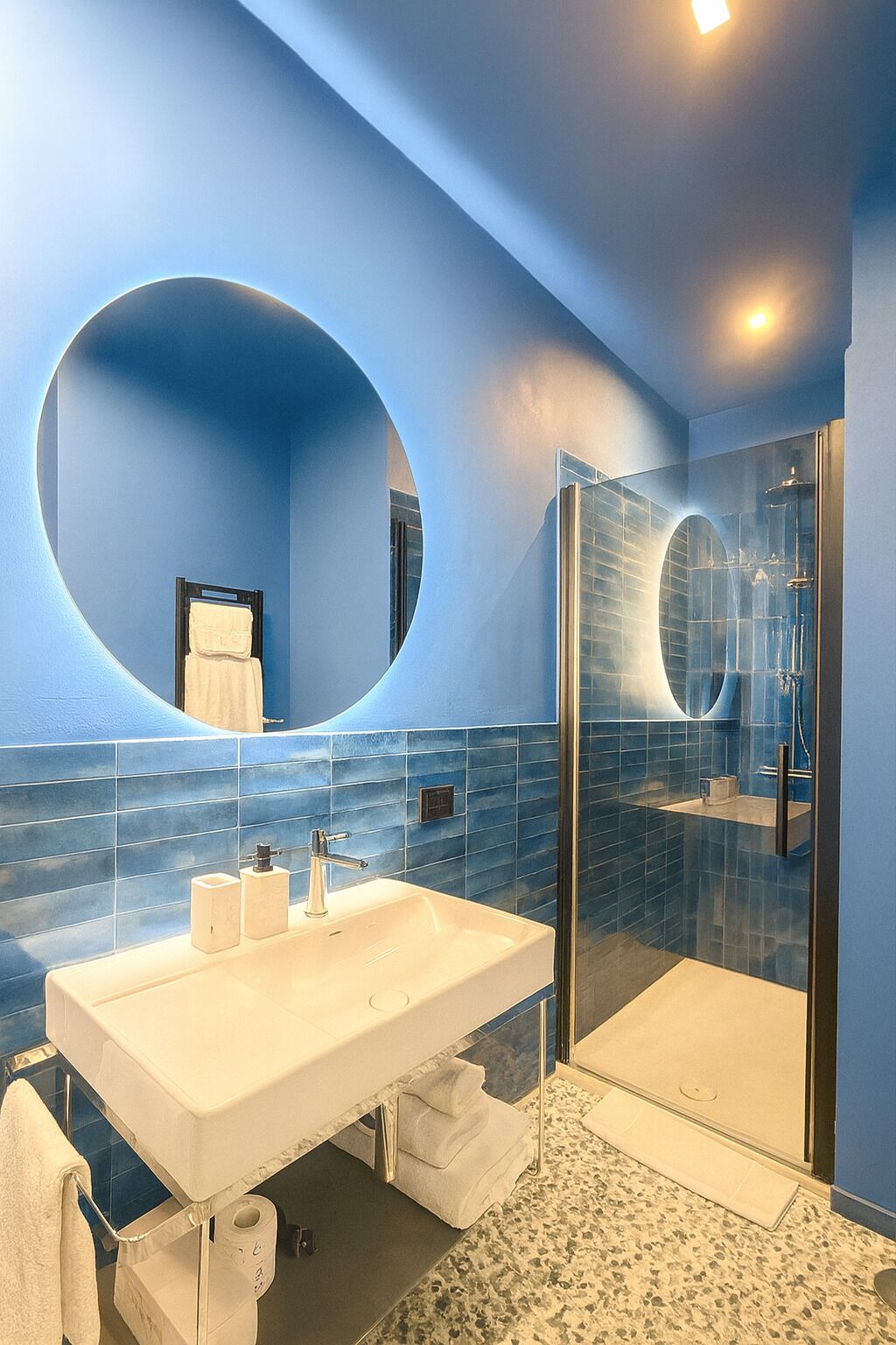 A modern bathroom with a large oval mirror, a glass-enclosed shower, and a white sink with a marble countertop.