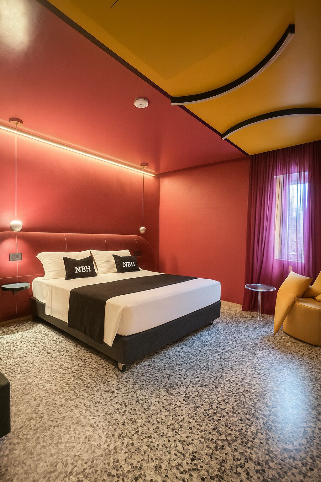 A hotel room with a bed, a small table, a chair, and a window with curtains.